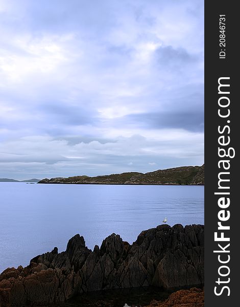 Scenic view in kerry ireland of bird on rocks and sea with mountains against a beautiful blue cloudy sky. Scenic view in kerry ireland of bird on rocks and sea with mountains against a beautiful blue cloudy sky