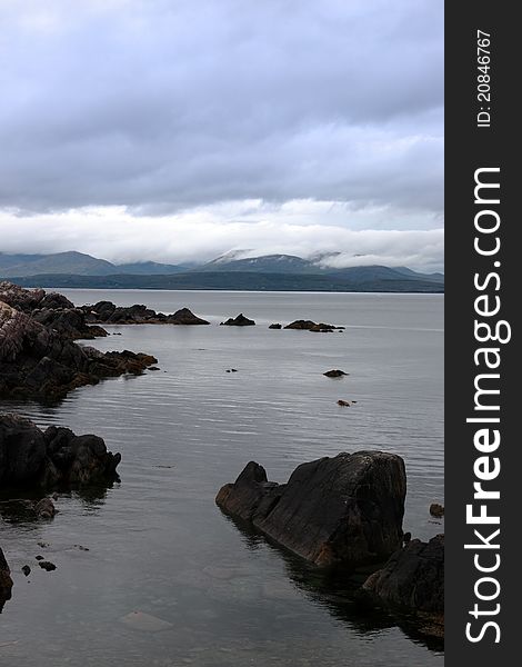 Scenic view in kerry ireland of rocks and sea with mountains against a beautiful blue cloudy sky. Scenic view in kerry ireland of rocks and sea with mountains against a beautiful blue cloudy sky