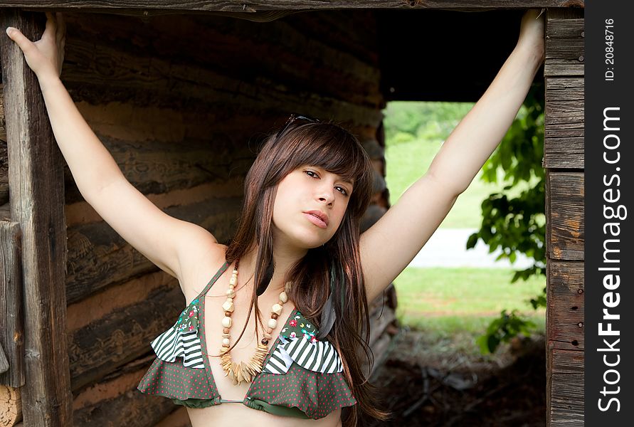 A portrait of a pretty young woman, wearing a ruffled bikini top and leaning against a wooden shed in a rural area. A portrait of a pretty young woman, wearing a ruffled bikini top and leaning against a wooden shed in a rural area