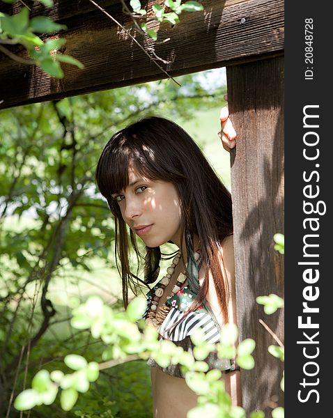 A portrait of a beautiful woman, leaning on a wooden structure and surrounded by trees. A portrait of a beautiful woman, leaning on a wooden structure and surrounded by trees