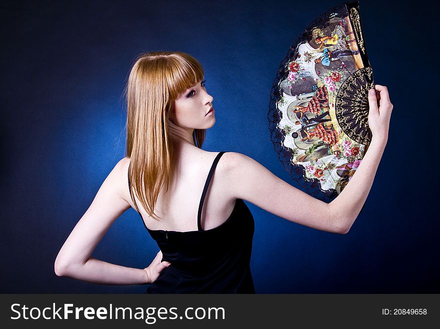 Beautiful young woman with a fan in studio ob the blue background