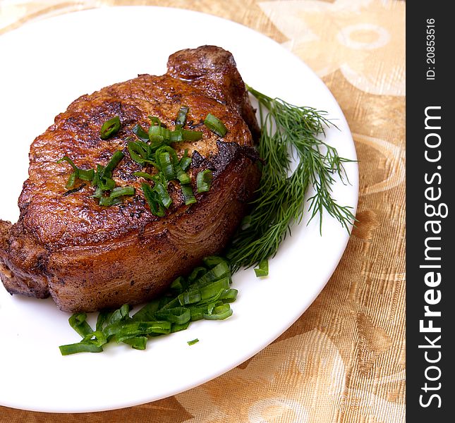 Big juicy well-done piece of meat lying on a white plate decorated with greenery. Big juicy well-done piece of meat lying on a white plate decorated with greenery