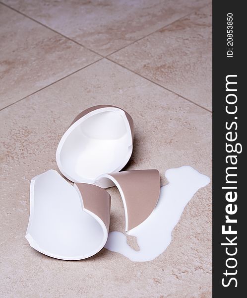 Broken fragments of cup and spilled milk on ceramic granite floor. Broken fragments of cup and spilled milk on ceramic granite floor