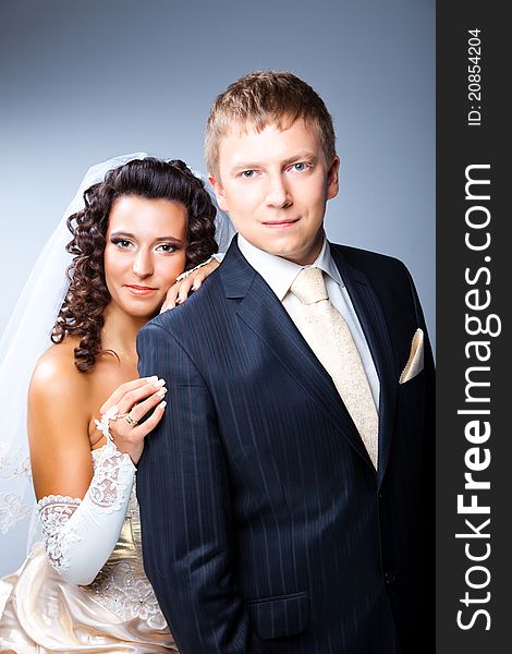 Studio portrait of young elegant enamoured just married bride and groom and embracing on grey background. Studio portrait of young elegant enamoured just married bride and groom and embracing on grey background