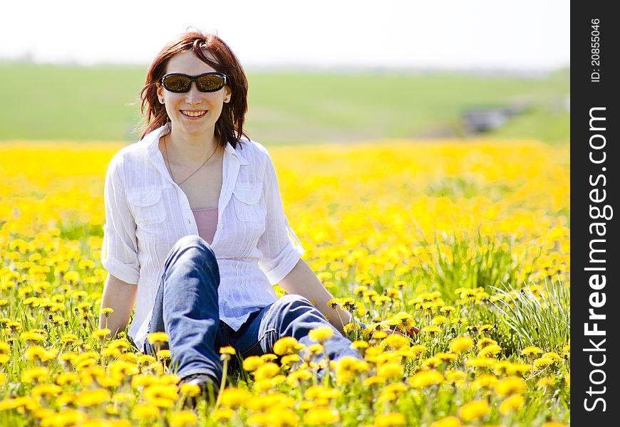 Beautiful young woman is sitting in a field with yellow dandelions. Beautiful young woman is sitting in a field with yellow dandelions
