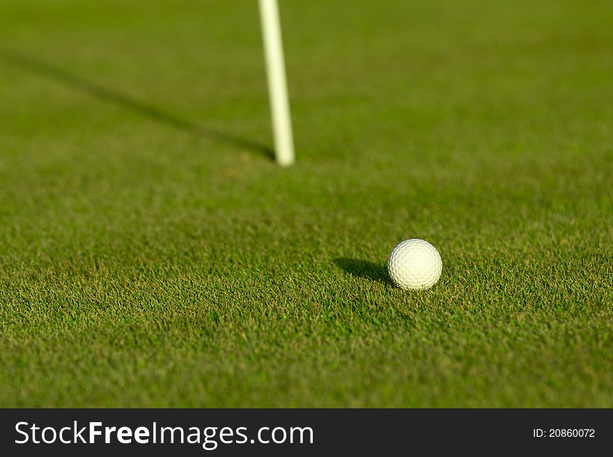 A golf ball near a hole with golf pole