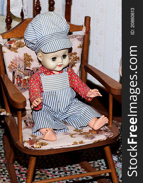 A child's old antique engineer boy doll sitting in a child's rocking chair. Shallow depth of field. A child's old antique engineer boy doll sitting in a child's rocking chair. Shallow depth of field.