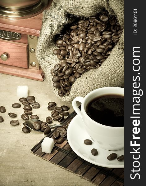 Cup of coffee and grinder with roasted beans on wooden background