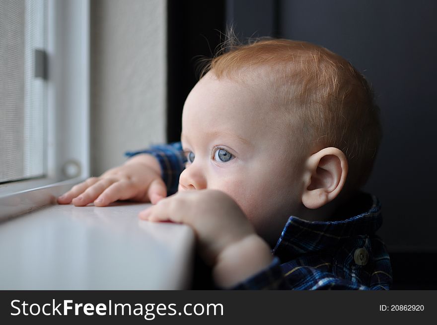 Red headed child boy with blue eyes looking out window. Red headed child boy with blue eyes looking out window.