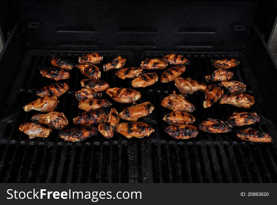 Several pieces of chicken barbecuing on the grill with char marks. Several pieces of chicken barbecuing on the grill with char marks.