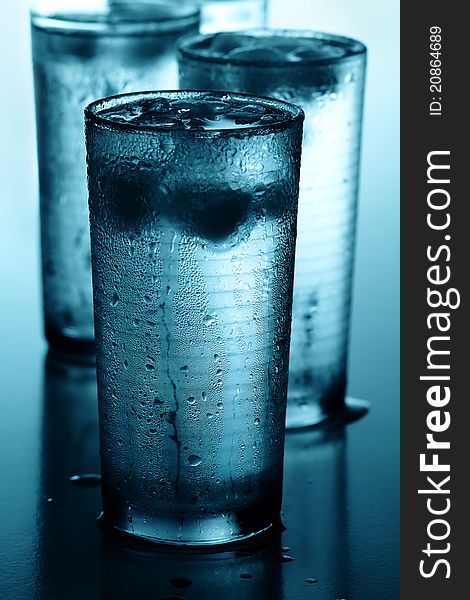 Glasses of cold water with ice cubes reflected on wet background