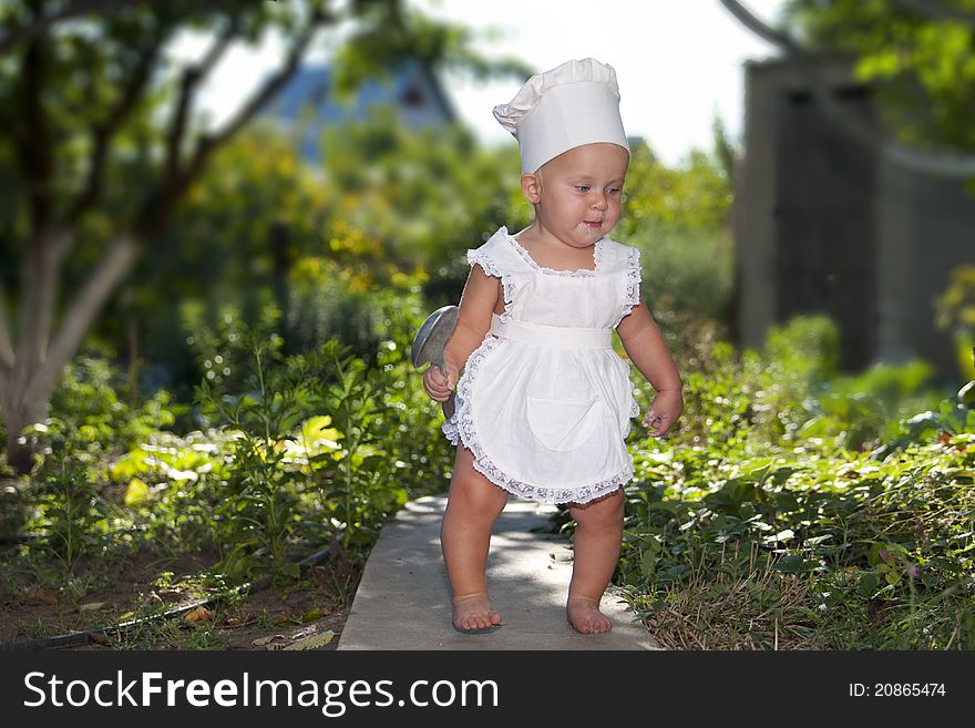 Cute little cook with big spoon goes to make dinner in the garden.