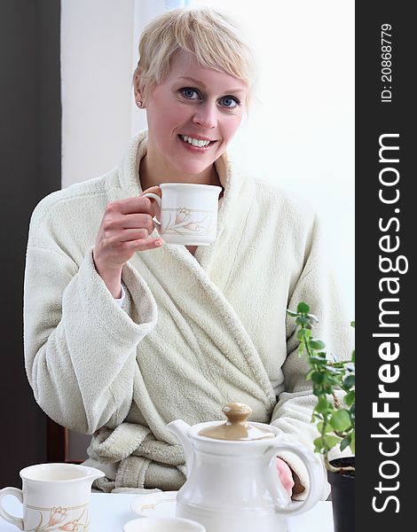 Image of a woman at home in the morning having breakfast sitting by the window having tea