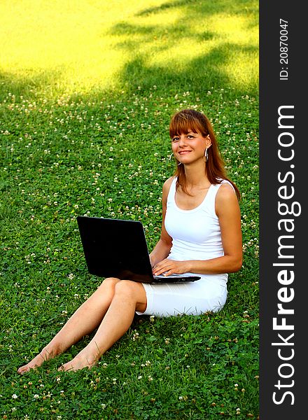 Woman on a green grass using laptop looking at the camera outdoor. Woman on a green grass using laptop looking at the camera outdoor