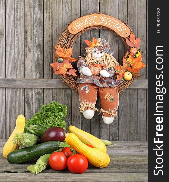 Harvested vegetables and fruits with a harvest wreath hanging on a weathered fence. Harvested vegetables and fruits with a harvest wreath hanging on a weathered fence