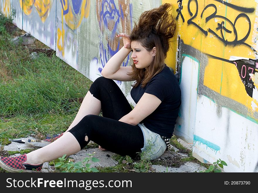 Punk girl sitting near graffiti wall