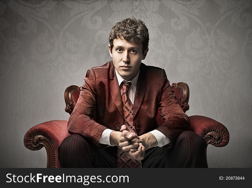 Portrait of a young elegant man sitting on a velvet armchair. Portrait of a young elegant man sitting on a velvet armchair