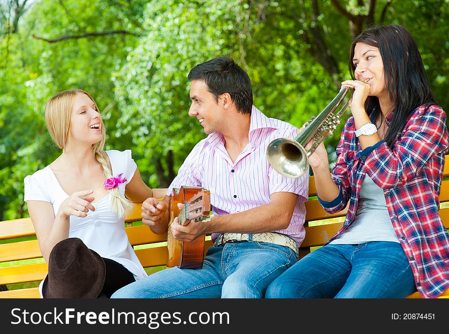 Young friends play the guitar and trumpet in the park