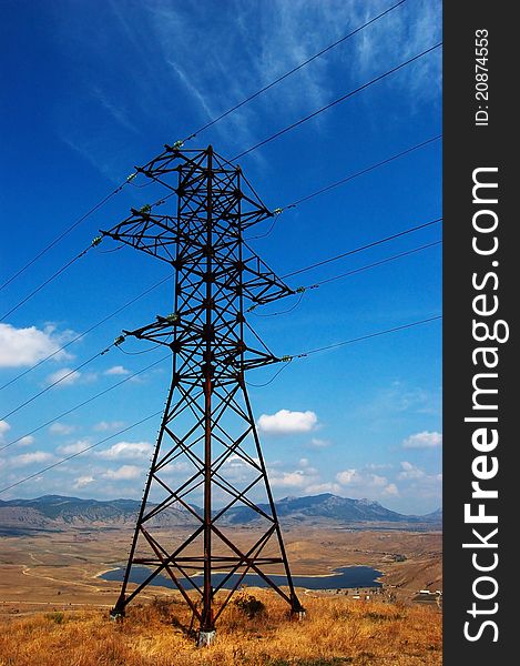 High-voltage line on background with clean blue sky with clouds,mountains and lake behinde. High-voltage line on background with clean blue sky with clouds,mountains and lake behinde
