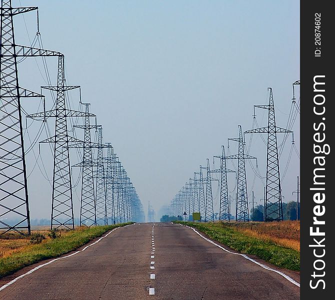 Highway between high-voltage power lines leads to horizon with blue sky on back
