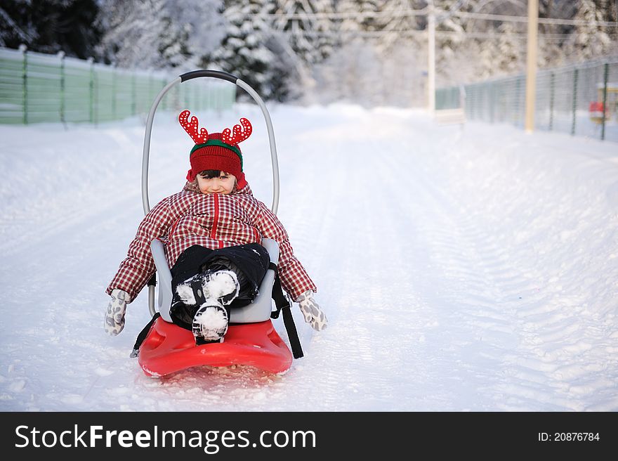 Adorable child girl in horned hat sled in snow