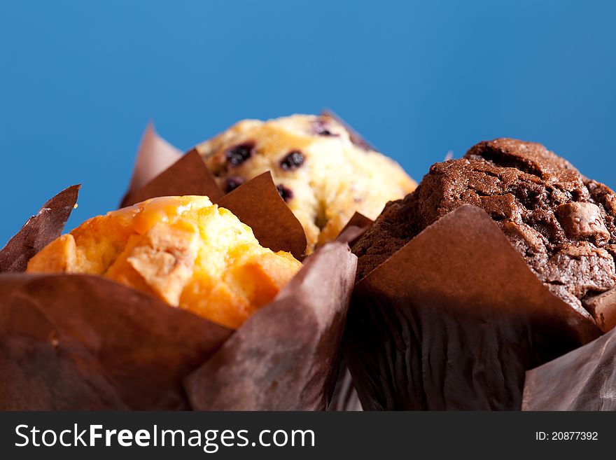 Three muffins on a blue background. Shallow depth of field with focus on the chocolate muffin. Three muffins on a blue background. Shallow depth of field with focus on the chocolate muffin.