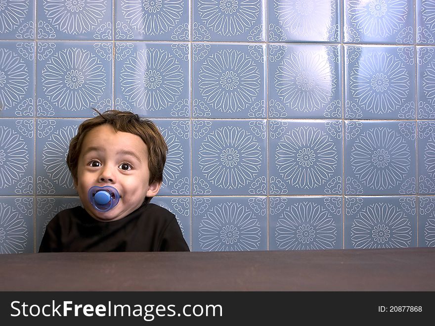 Portrait of a little boy smiling. He is sitting at a table in front of a very retro looking wall. Portrait of a little boy smiling. He is sitting at a table in front of a very retro looking wall.