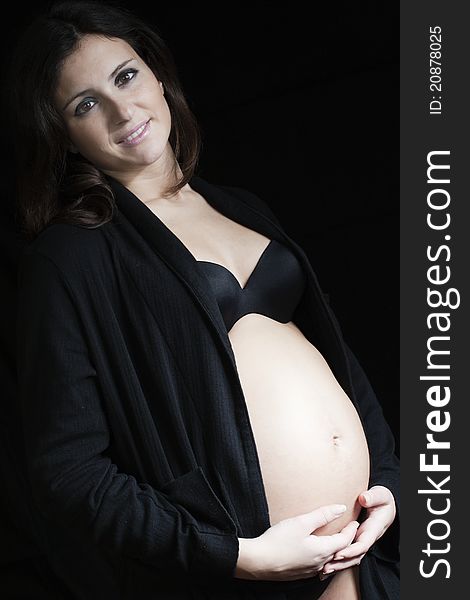 Pregnant woman with a black robe standing on a black background. Pregnant woman with a black robe standing on a black background