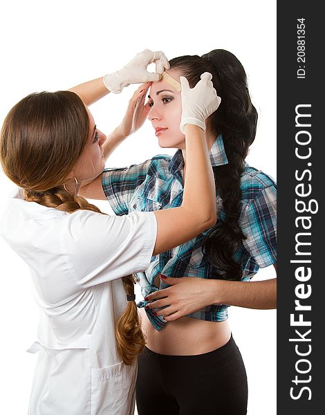 Beautiful nurse in white medical gown glues sticking plaster on his forehead to patient on white background. Beautiful nurse in white medical gown glues sticking plaster on his forehead to patient on white background