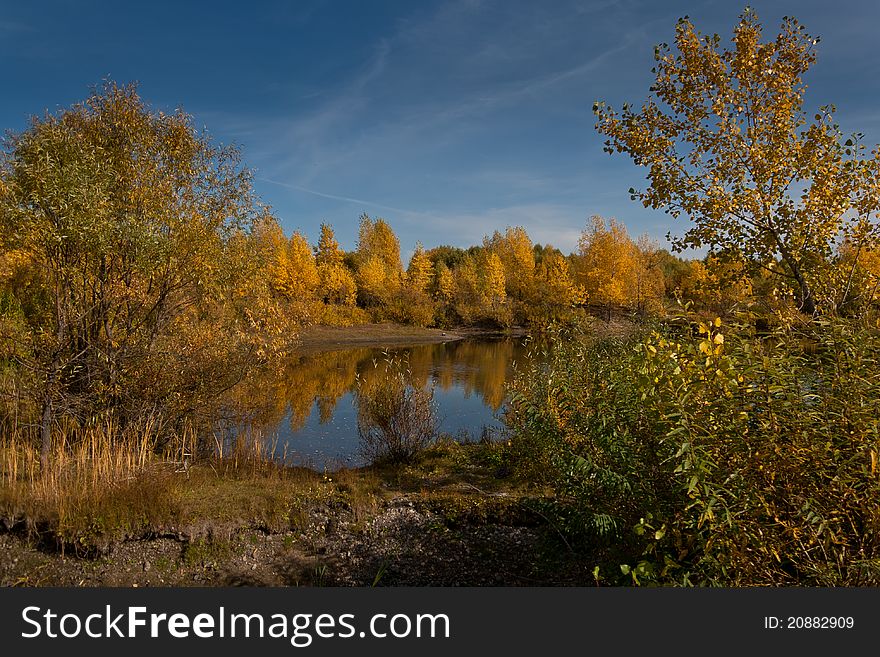 Autumn trees with the turned yellow foliage are reflected in dark blue lake, over them the blue sky. Autumn trees with the turned yellow foliage are reflected in dark blue lake, over them the blue sky.