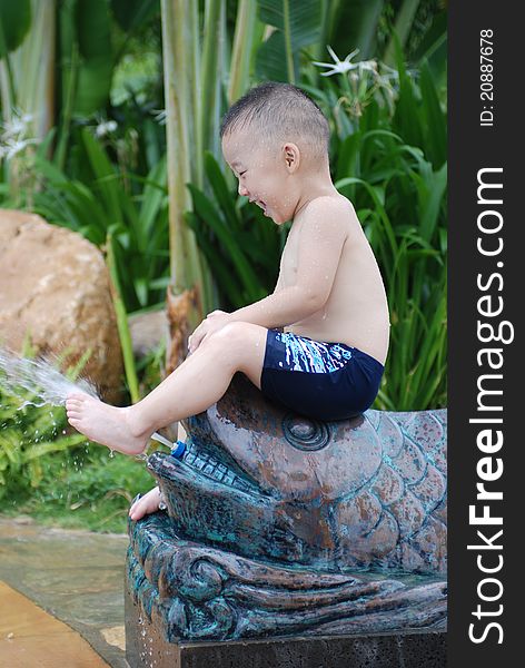 Little boy plays with water jet from fish-shape hose outdoors. Little boy plays with water jet from fish-shape hose outdoors