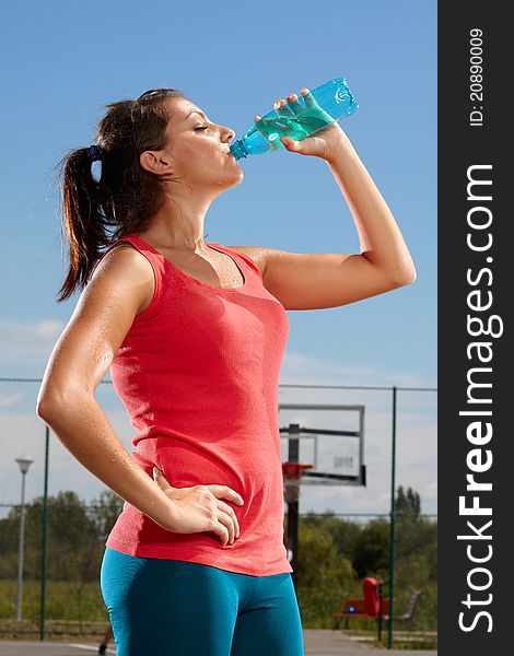 Young woman drinking mineral water on a basketball court. Young woman drinking mineral water on a basketball court