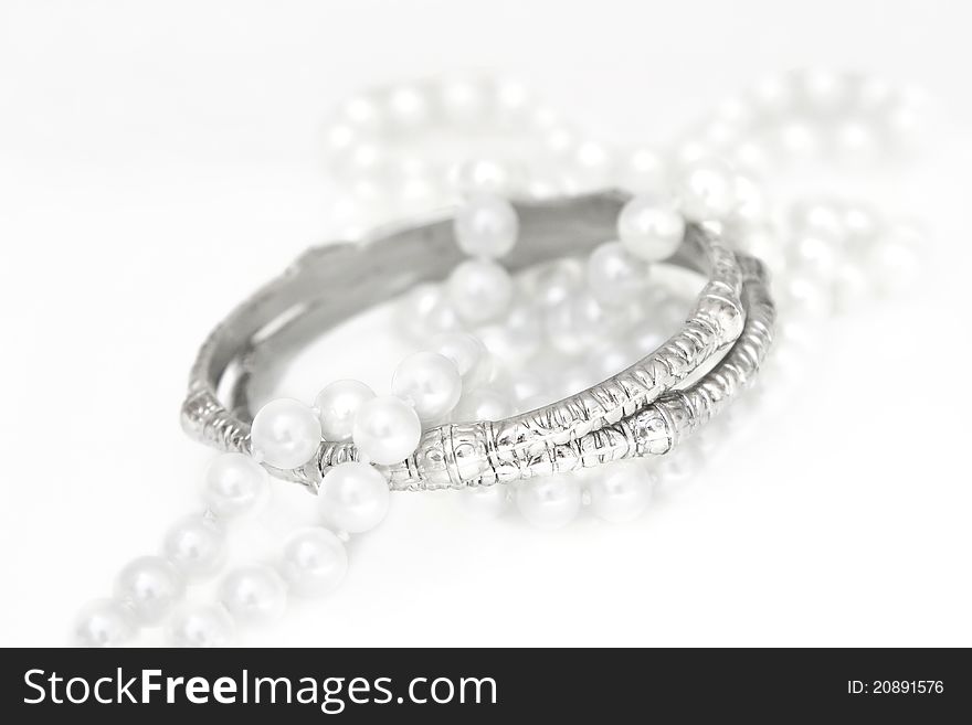A set of accessories consisting of two silver bracelets and imitation pearls on white. A set of accessories consisting of two silver bracelets and imitation pearls on white.