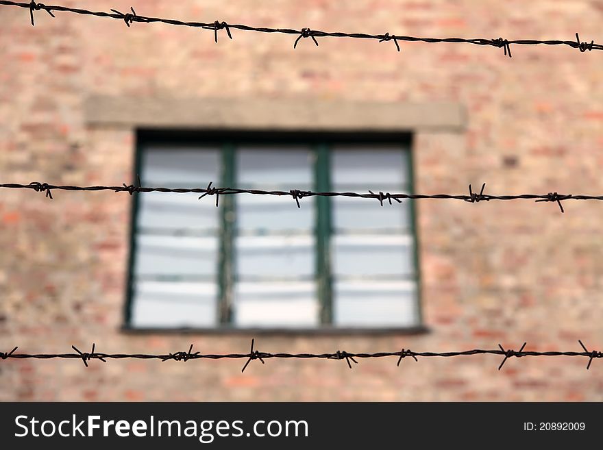 Brick building's wall with window behind barbed wire fence. Brick building's wall with window behind barbed wire fence.