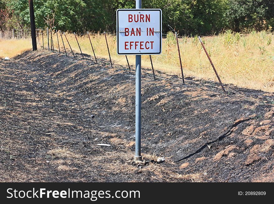 Burn ban sign in charred drainage ditch in central Texas during drought.