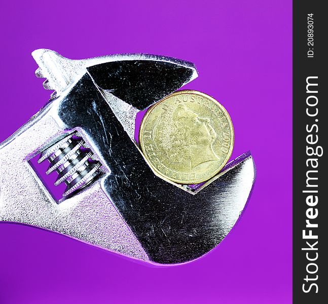 A Gold Dollar Coin in a being squeezed in a silver adjustable spanner, against a purple background asking the questions how is your household budget?. A Gold Dollar Coin in a being squeezed in a silver adjustable spanner, against a purple background asking the questions how is your household budget?