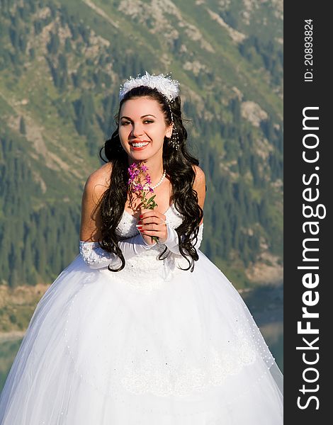 Smiling bride with flowers in the mountains