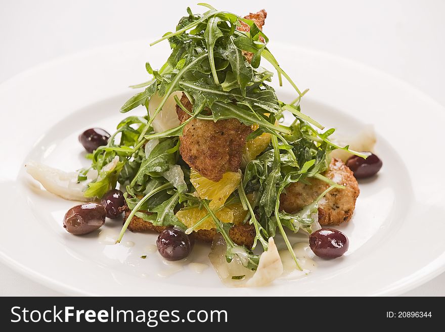 Crumbed chicken with rocket,onions,olives and oranges on a plate