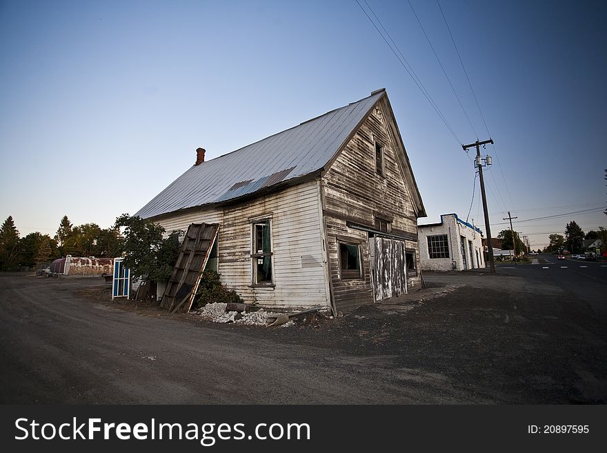 An aging and abandoned building sits in a nearly empty lot in the evening hours.