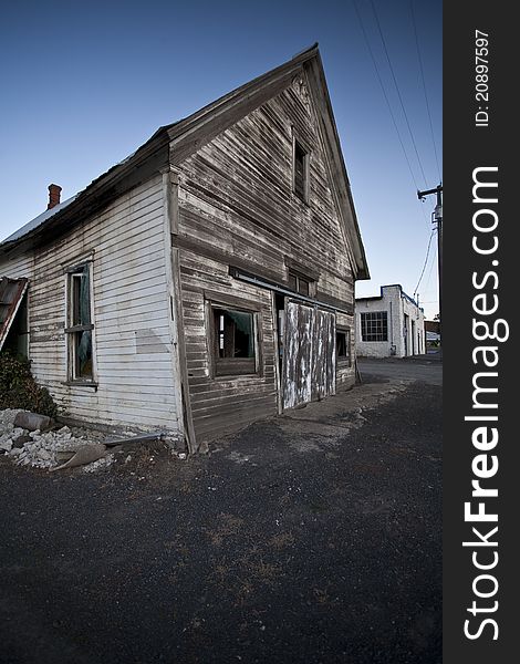 An aging and abandoned building sits in a nearly empty lot in the evening hours.