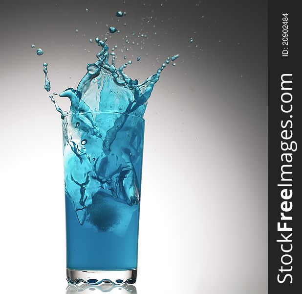 Splashes of water of dark blue color from a glass. In a glass the ice piece falls. Splashes of water of dark blue color from a glass. In a glass the ice piece falls