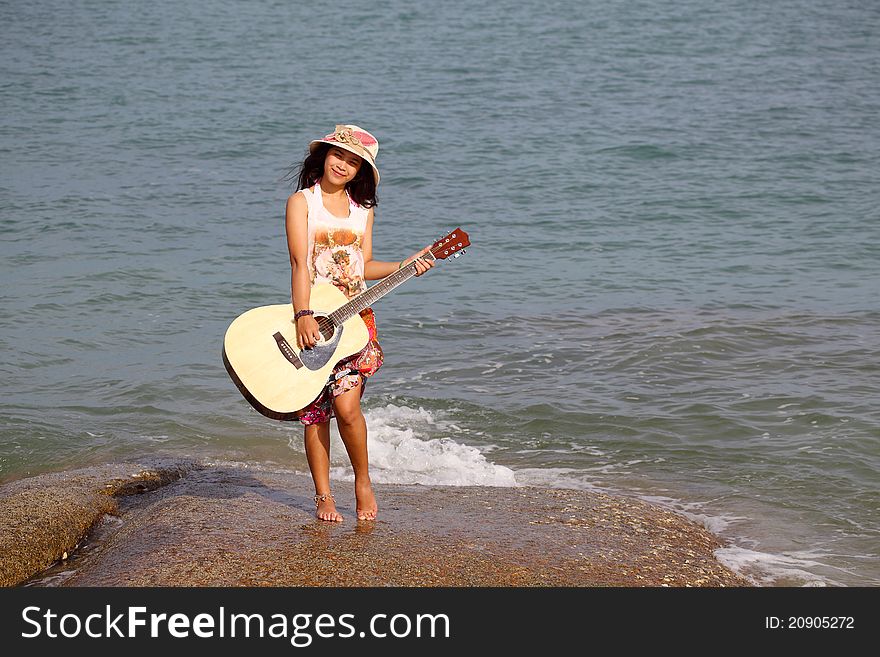 Pretty young woman playing guitar on stone near beach. Pretty young woman playing guitar on stone near beach