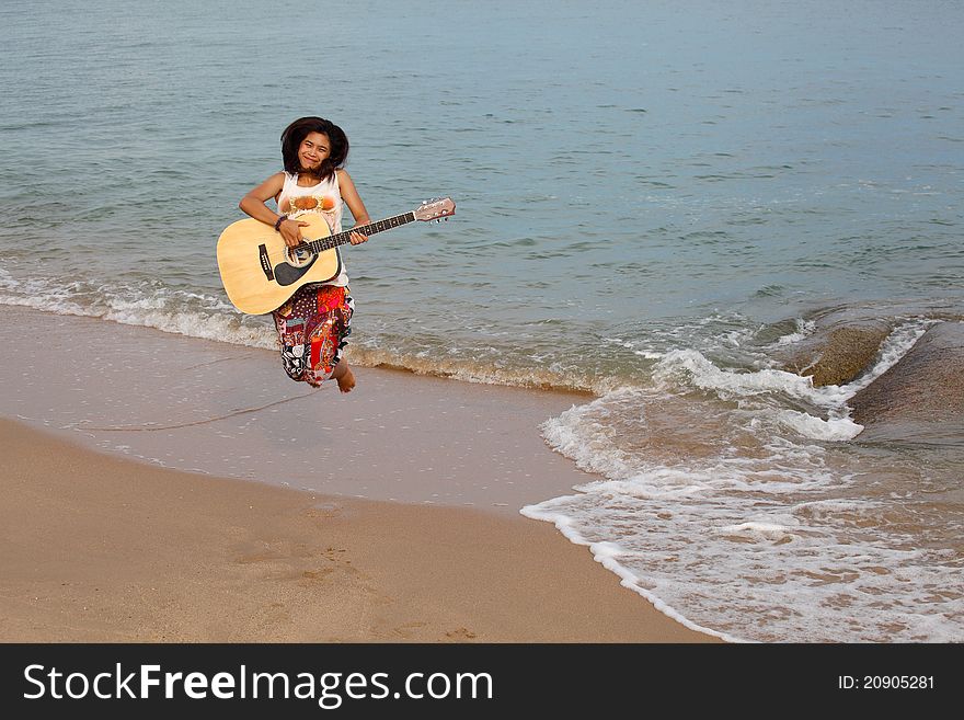 Happy girl jumping with guitar on beach