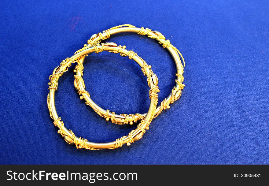 Two gold designed bangles on blue background. Two gold designed bangles on blue background