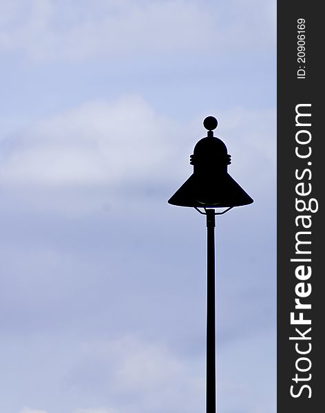 A street lamp silhouette againt a slightly overcast blue sky.