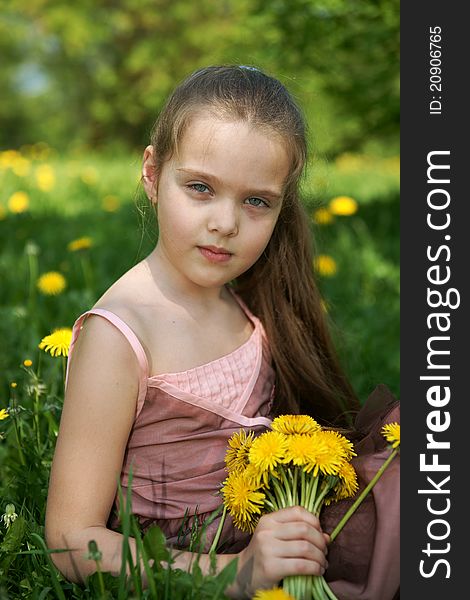 Little girl sits on a glade with dandelions
