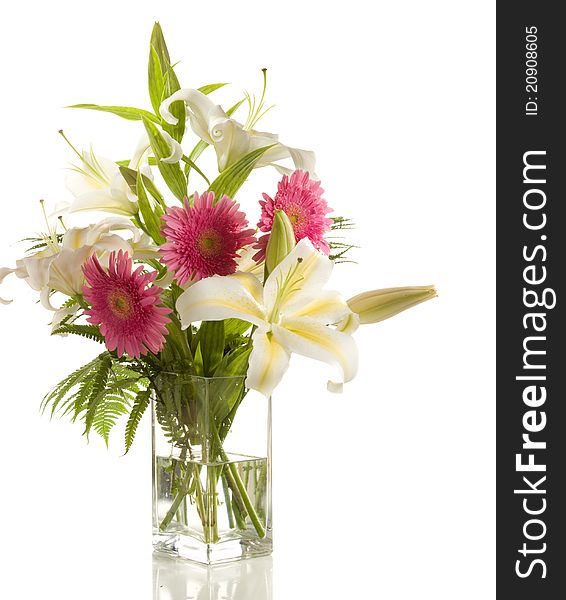 A bunch of lilies and gerberas in the transparent vase on the white background