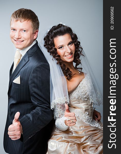 Studio portrait of young beautiful happy just married bride and groom gesticulating on gray background. Studio portrait of young beautiful happy just married bride and groom gesticulating on gray background