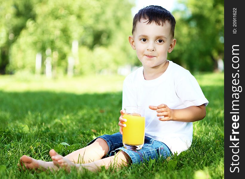 Portrait of a happy little boy sitting with a glass of orange juice in summer park. Portrait of a happy little boy sitting with a glass of orange juice in summer park