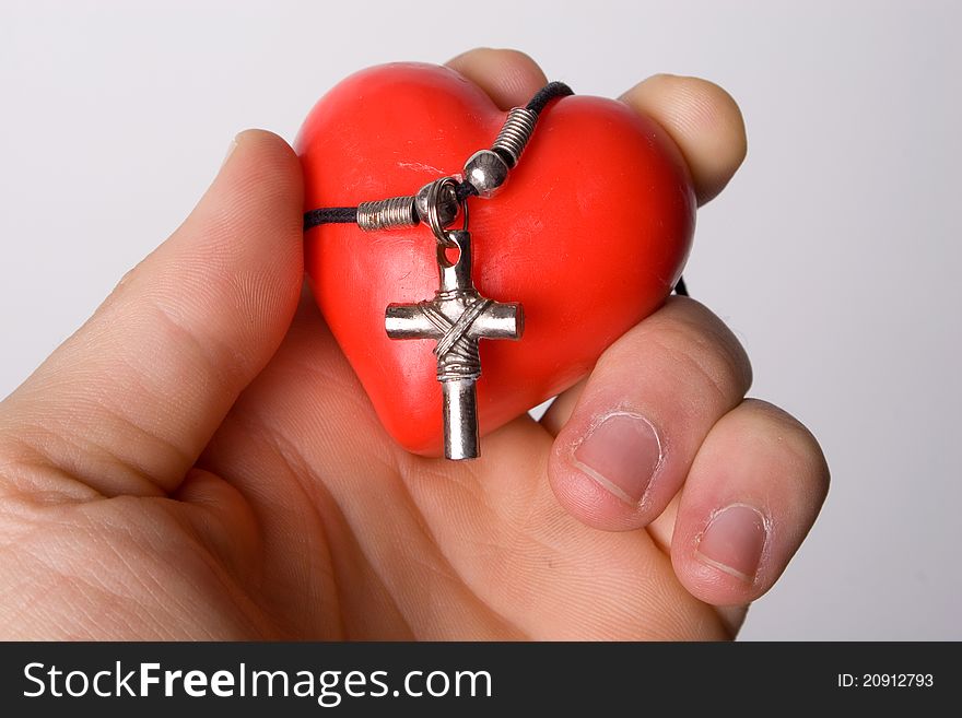 A man holding a wax heart and silver crucifix on a chain. A man holding a wax heart and silver crucifix on a chain